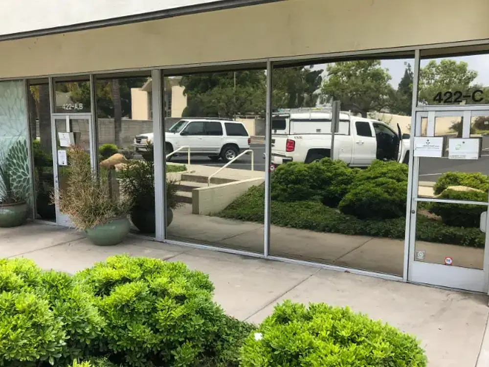 Reflective solar film on a suite of storefront windows, mirroring the parking lot and planting outside.